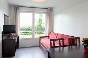 Um quarto com cama, televisão, mesa e janela com cortinas.