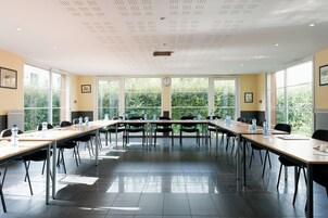 Uma sala de conferências com mesas compridas, cadeiras, garrafas de água e um relógio na parede.