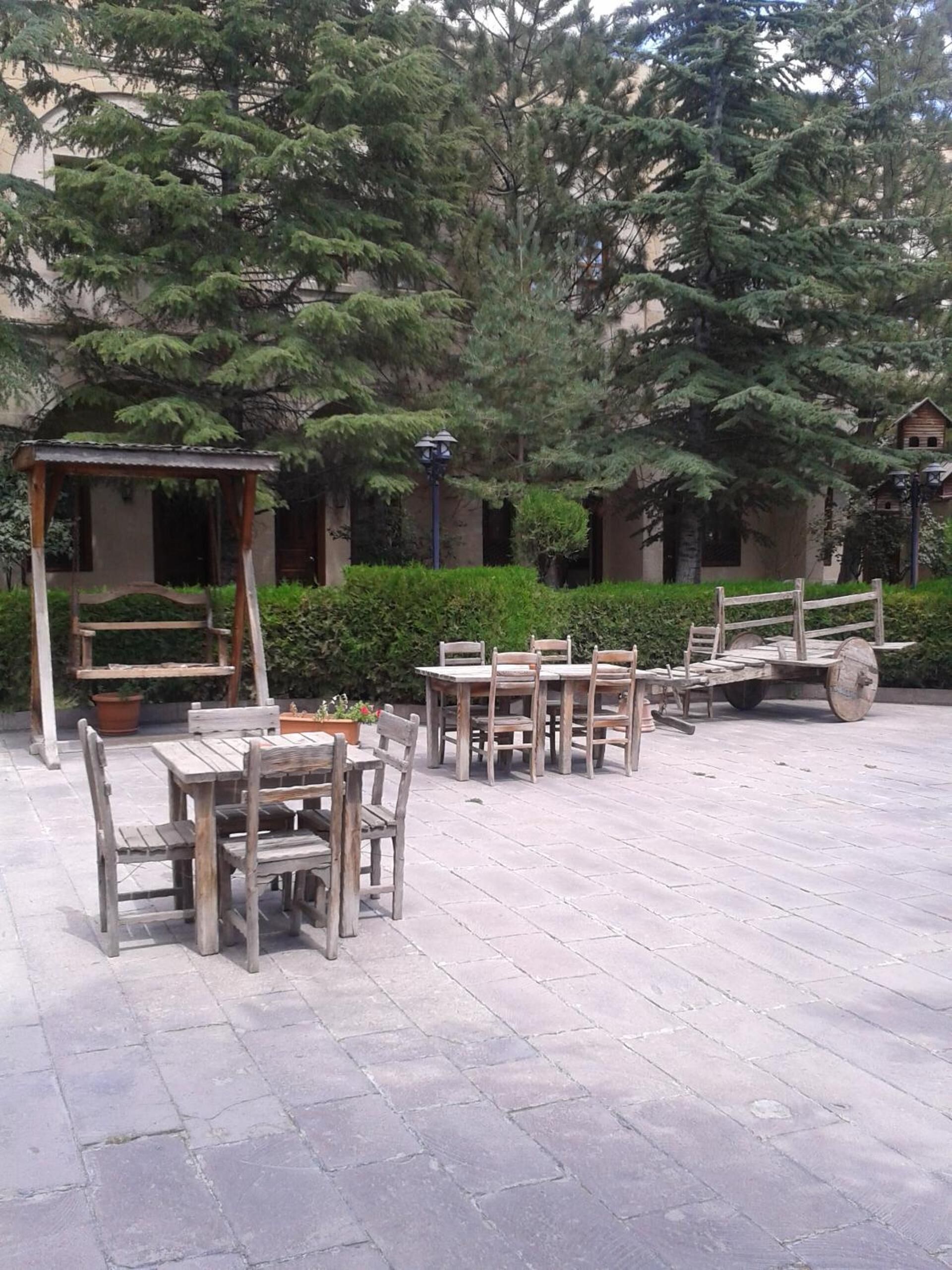 Un patio al aire libre con suelo de piedra, mesas y sillas de madera, una pérgola de madera y un seto.