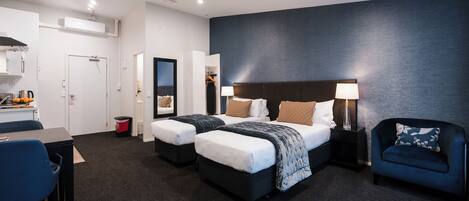 A hotel room with two beds, a desk, a chair, a wardrobe, and a nightstand with a lamp.
