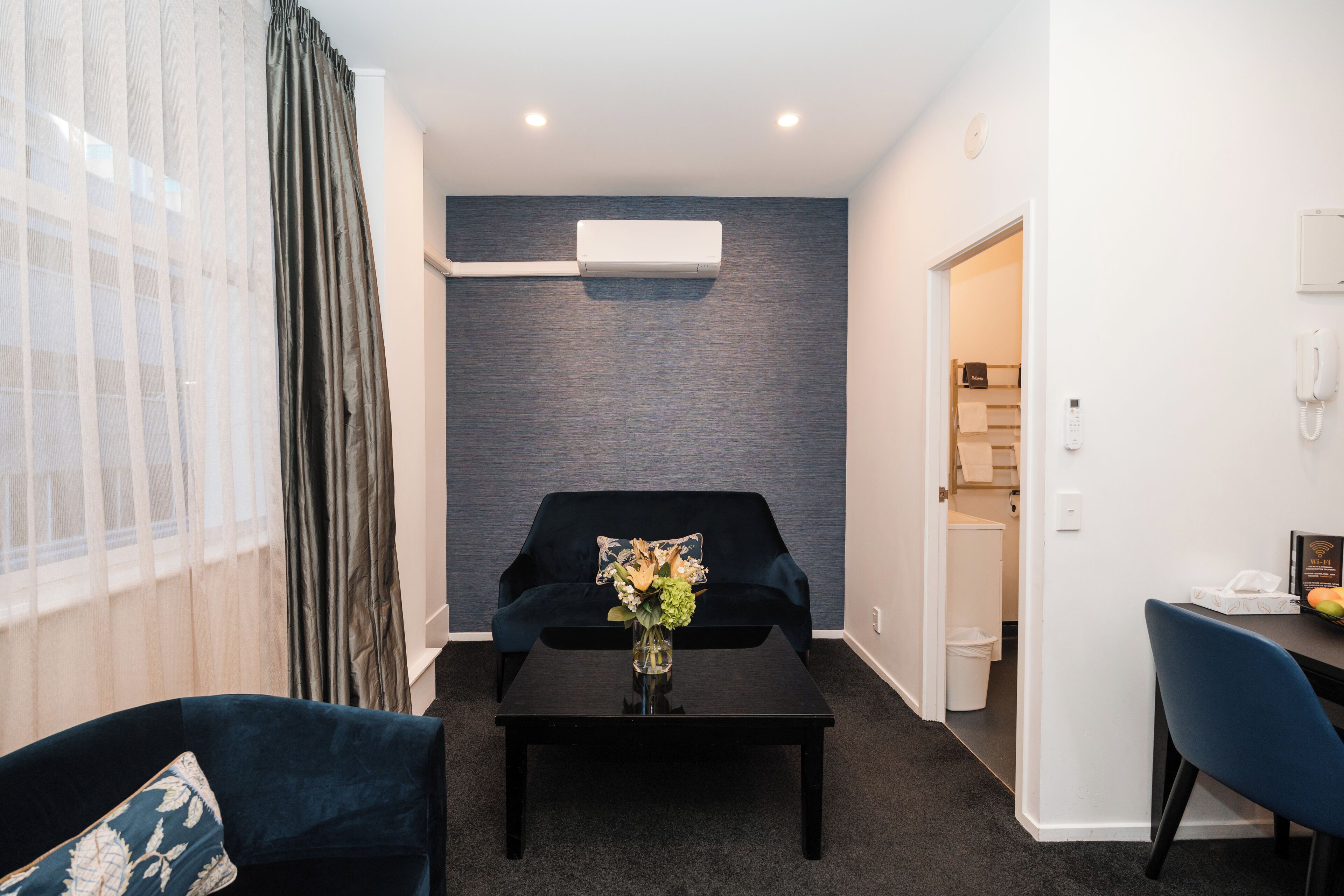 A modern living room with a dark blue sofa, a black coffee table with a vase of flowers, and a grey textured wall.