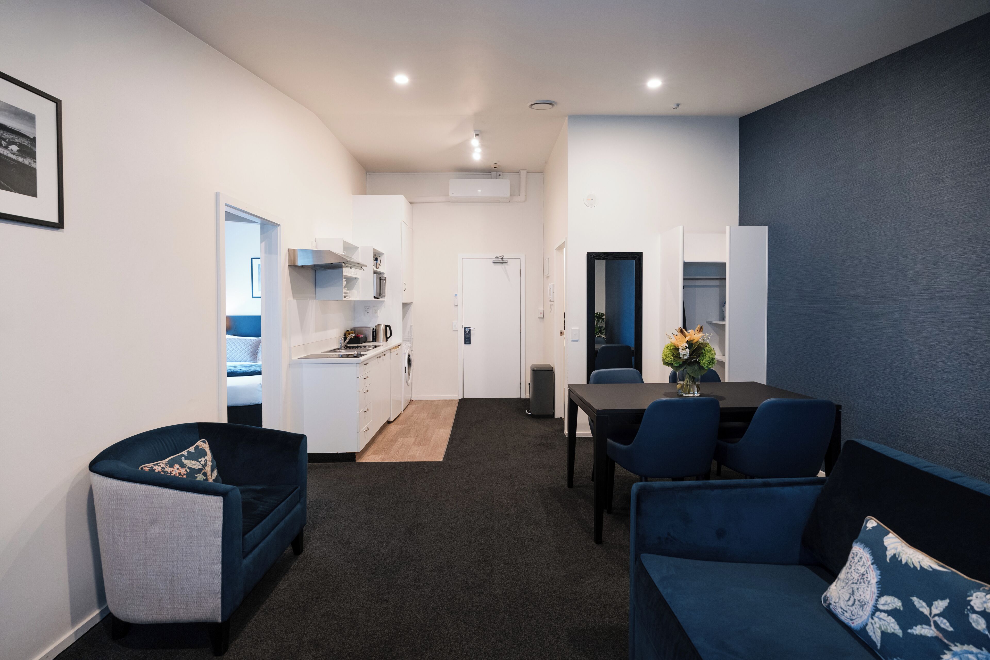 A modern living room with a sofa, a dining table with chairs, and a kitchen area in the background.