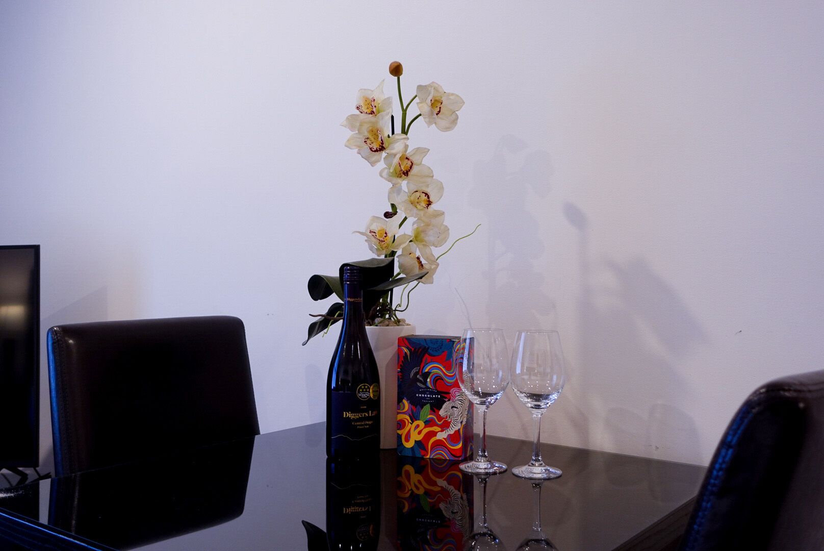 A table with a bottle of wine, two wine glasses, and a box of chocolates.