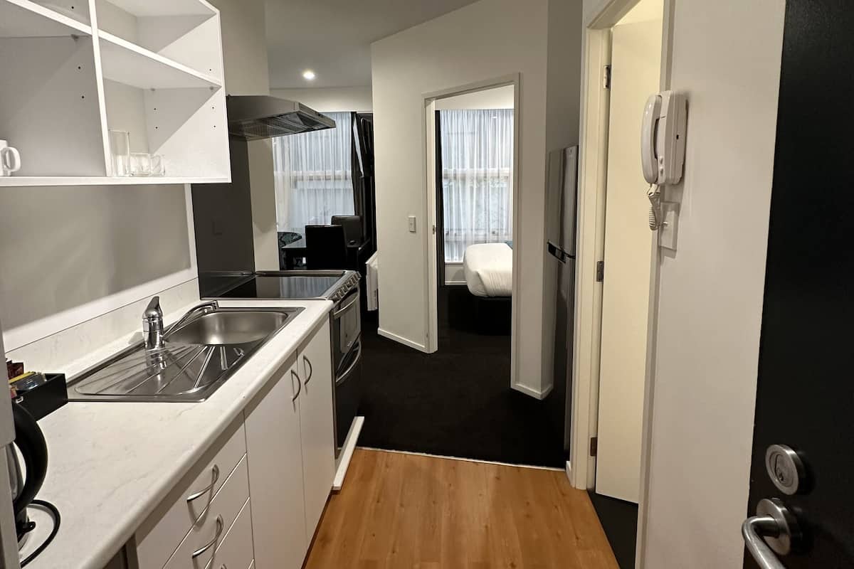 Una cocina compacta con lavabo, cocina y armarios, que da paso a un dormitorio con cama y un baño con inodoro y lavabo.