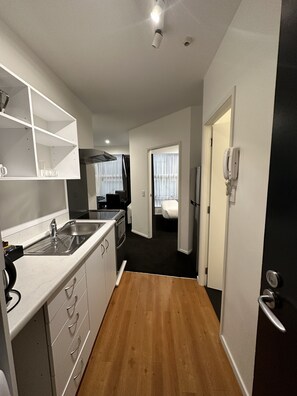 Modern kitchen with oven, microwave, and stainless steel sink, adjacent to a cozy bedroom with a white bed.