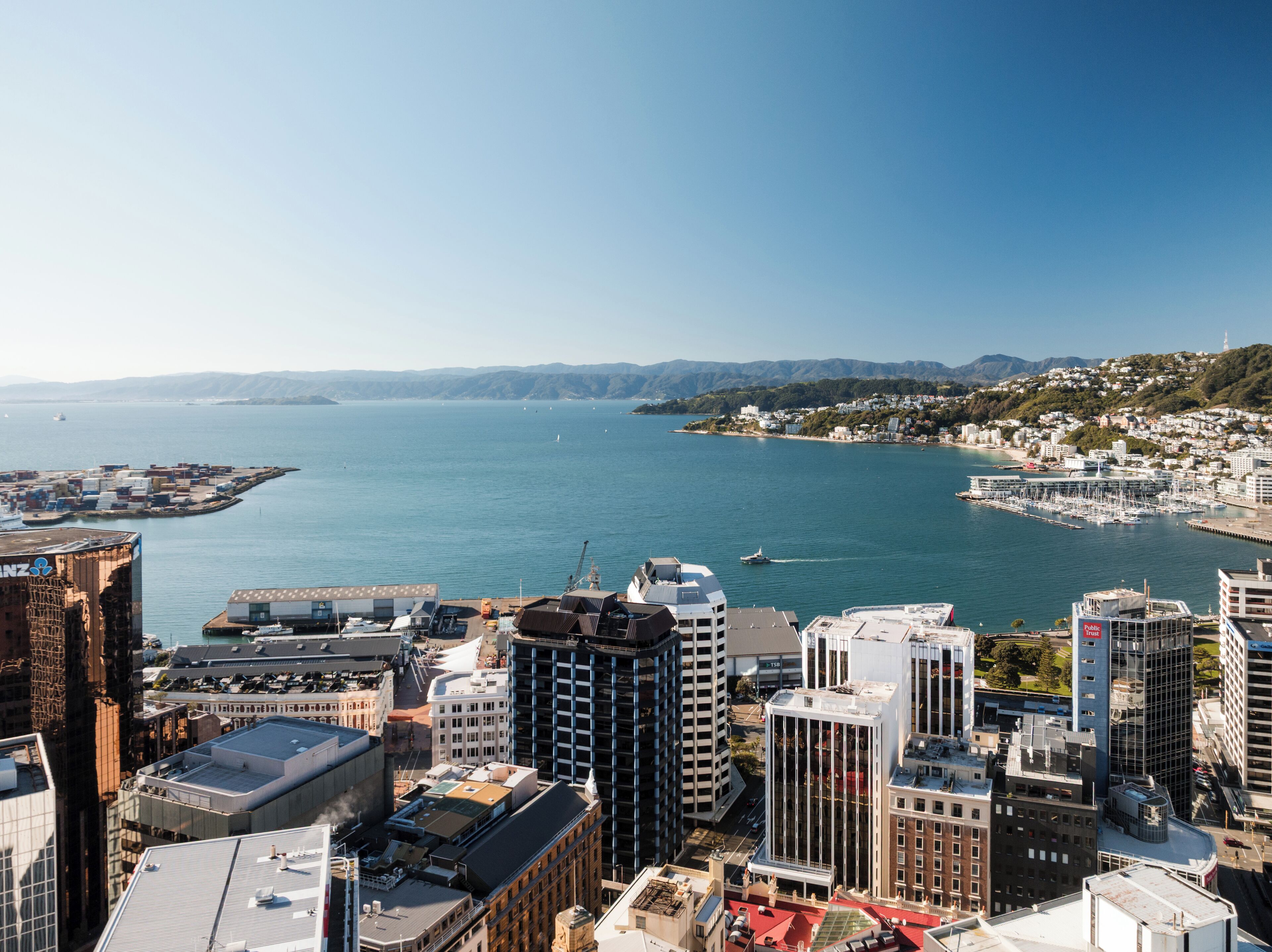 A coastal cityscape with high-rise buildings, a marina, and a clear view of the sea.