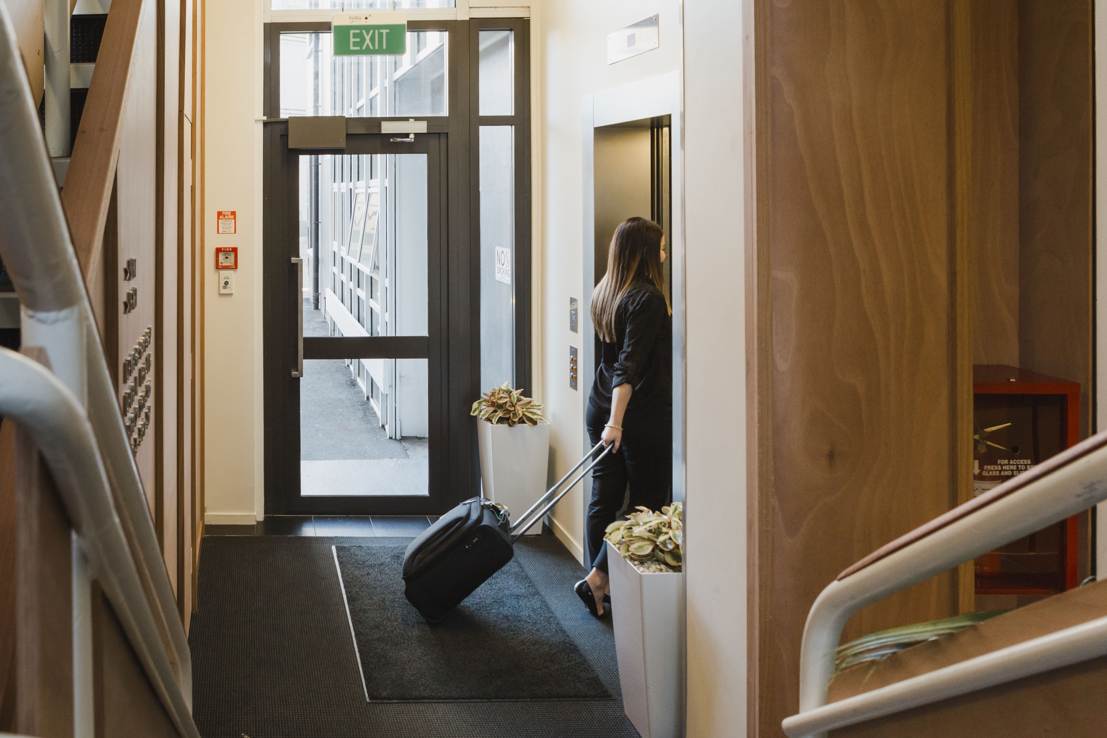 A hotel entrance with an exit sign, a luggage trolley, and a staircase.