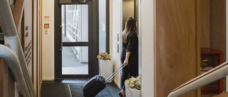 A hotel entrance with an exit sign, a luggage trolley, and a staircase.