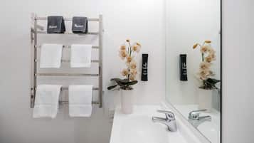 Un baño con lavamanos blanco, dos toalleros con toallas blancas y negras, y un florero con orquídeas.
