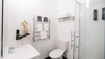 A modern bathroom with a white sink, toilet, and shower. There are towels and toiletries on shelves.