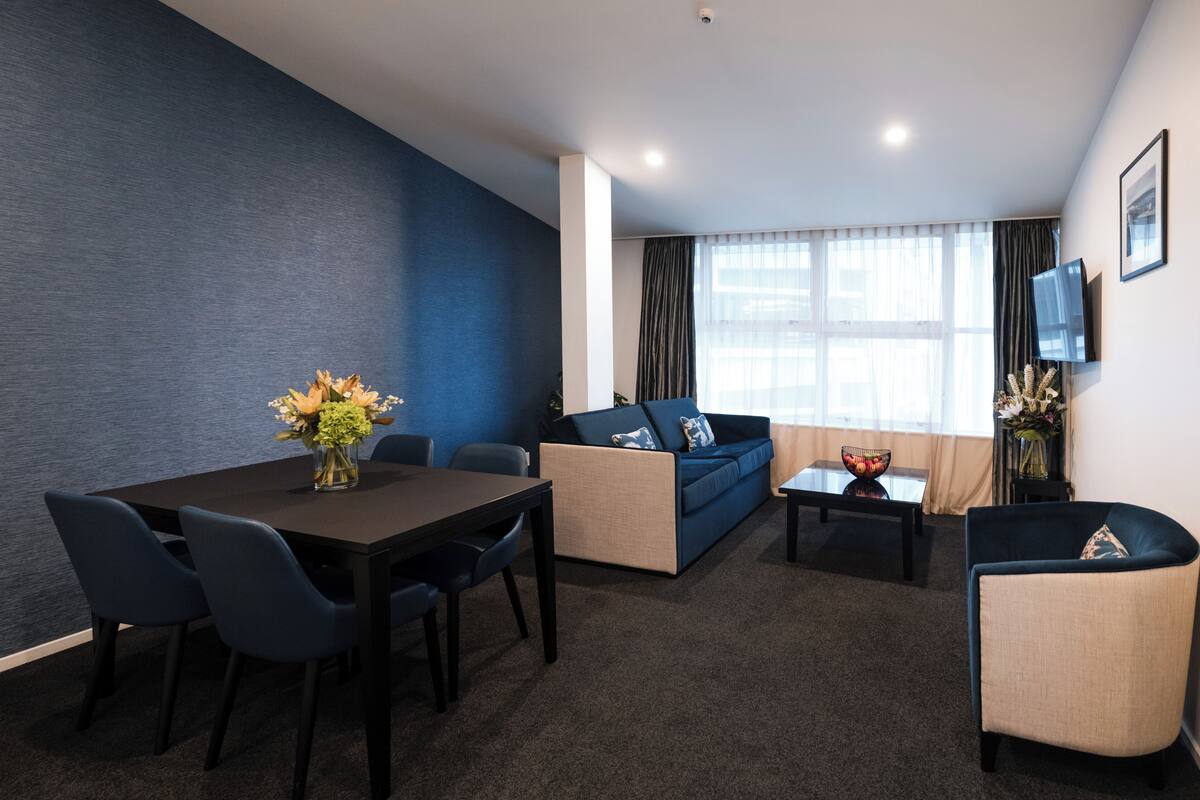 Una sala de estar moderna con una pared azul oscuro, un sofá, una mesa de centro y un televisor montado en la pared.