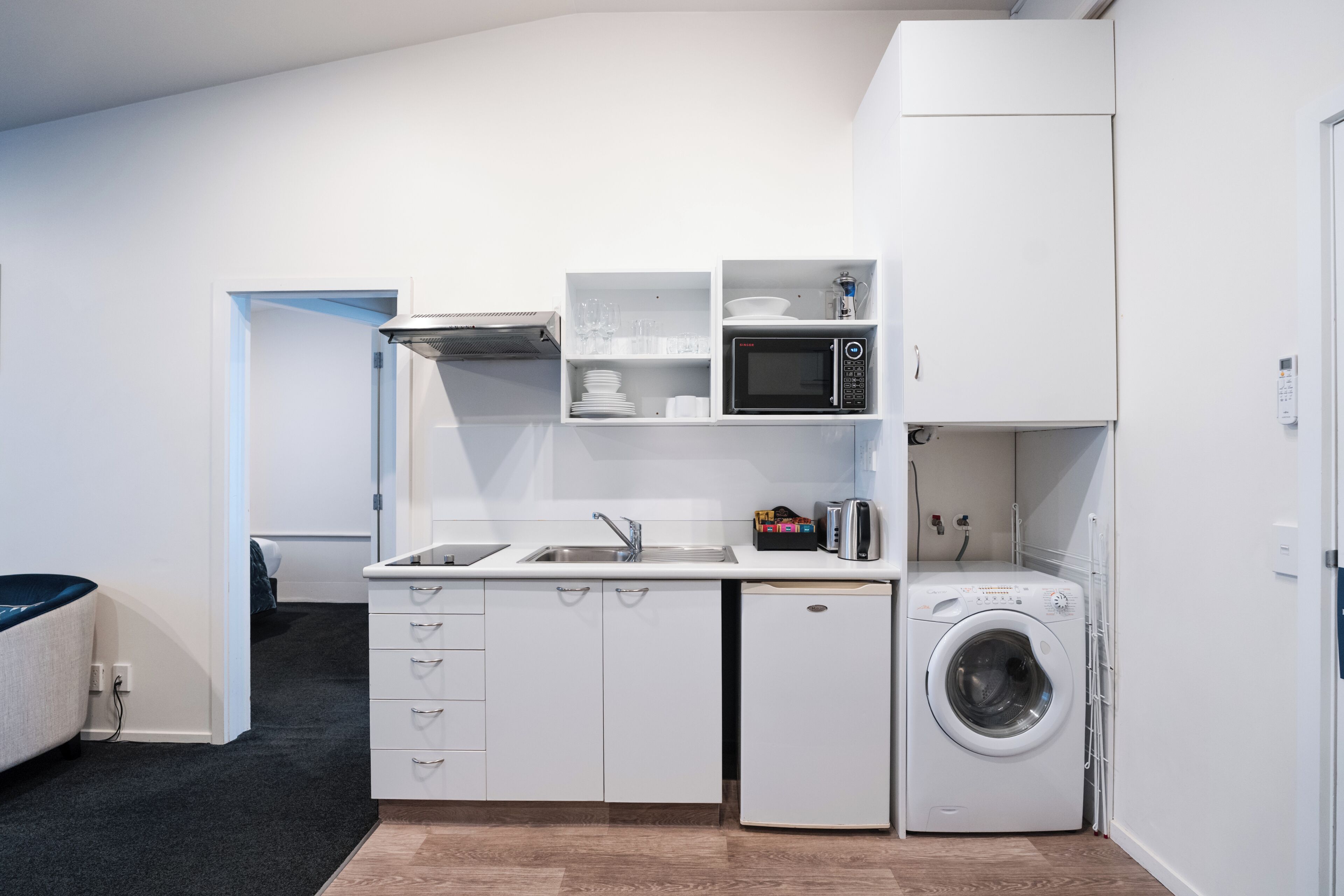 Een kleine keuken met een magnetron, spoelbak en een ingebouwde wasmachine.