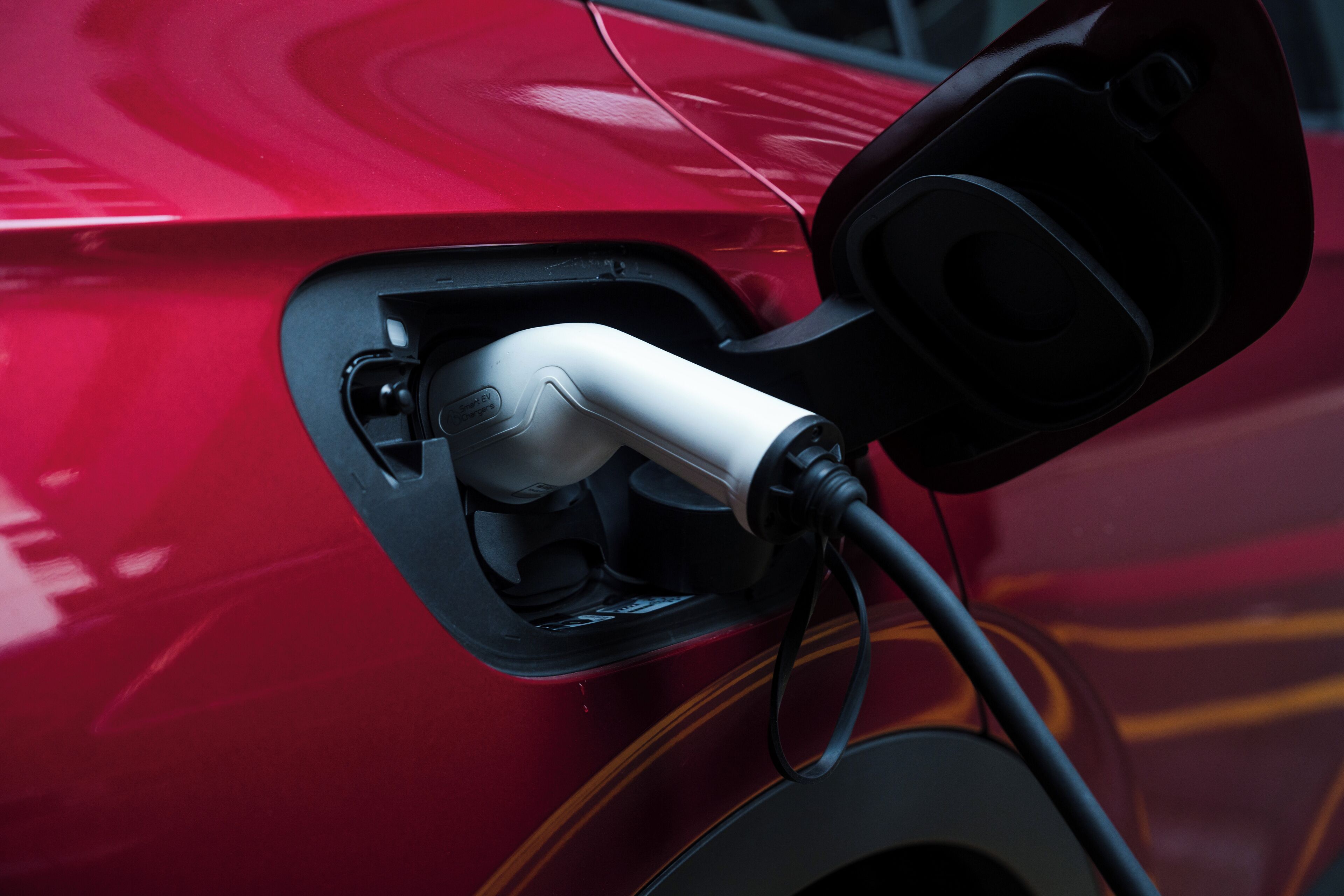 Ein rotes Auto mit angeschlossenem Ladekabel an einer Ladestation.