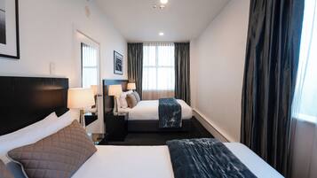 A hotel room with a large bed, a smaller bed, a nightstand with a lamp, a framed picture on the wall, and a window with curtains.