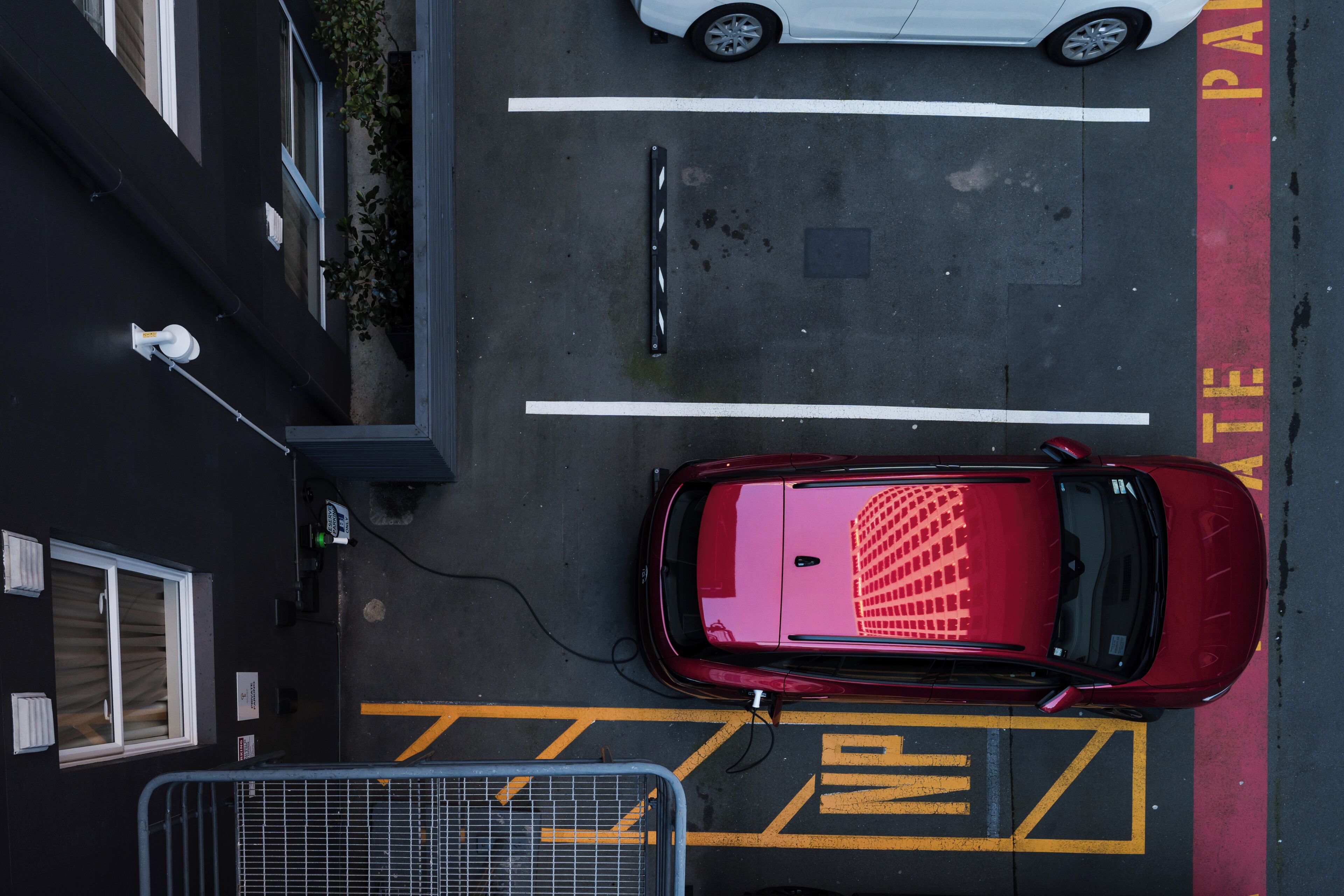 A parking area with marked spaces, a red car, and a building with windows and a security camera.