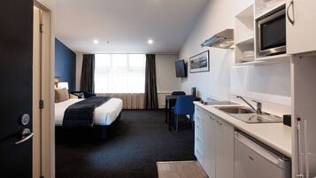 A hotel room with a bed, a desk, a chair, a kitchenette, and a TV.