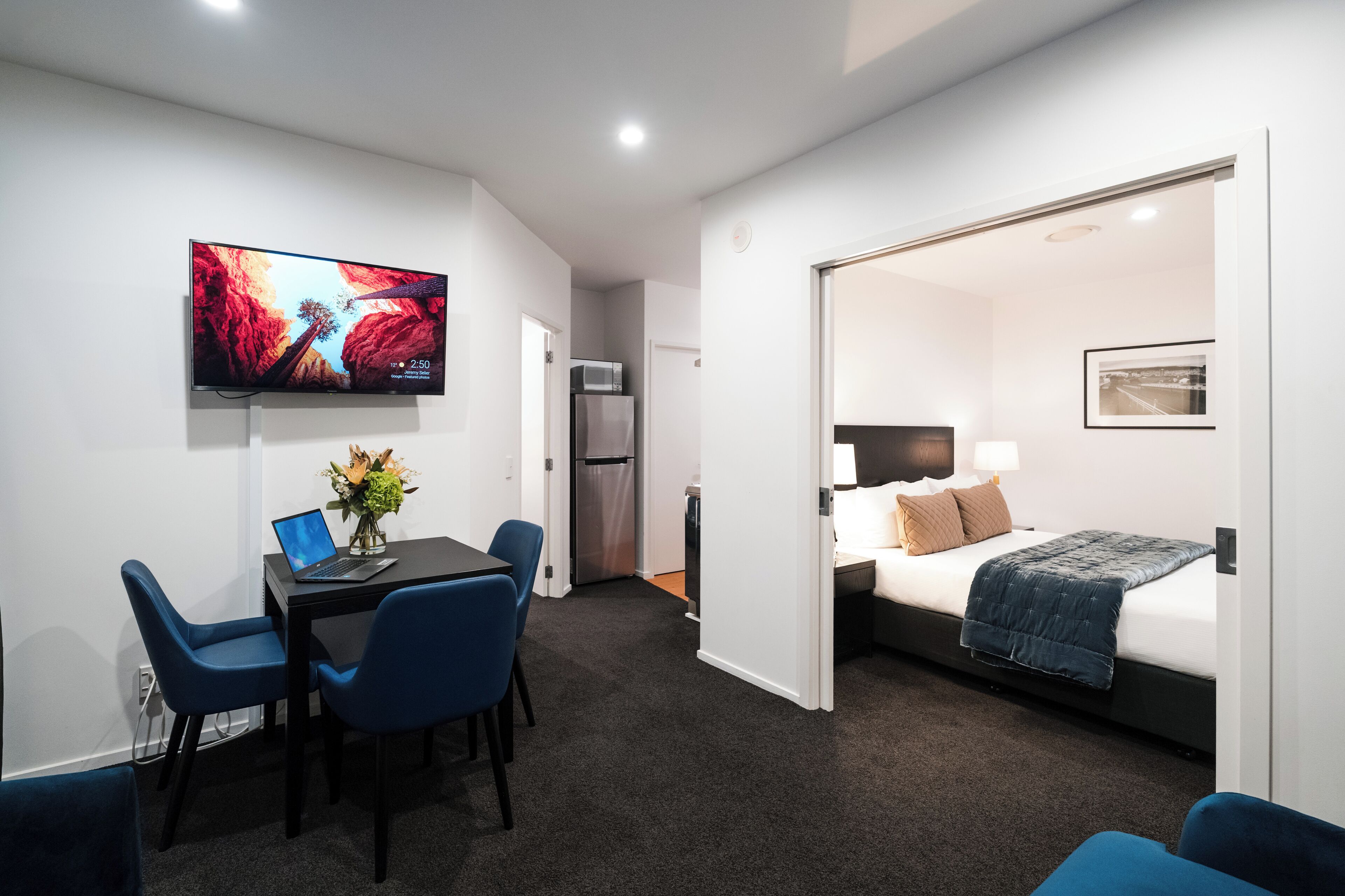 Ein Hotelzimmer mit Schreibtisch, Stühlen, Fernseher, Bett und einer Tür zu einem anderen Raum.