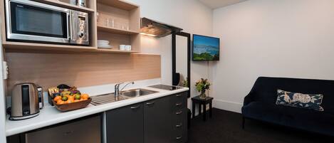 A compact kitchen with a microwave, kettle, and fruit bowl. There's a sofa and a small table with a plant.