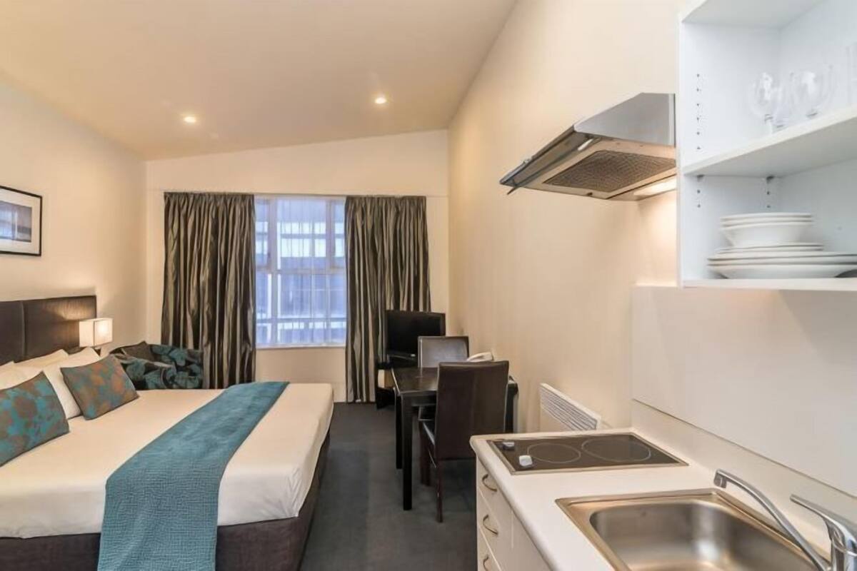 Habitación de hotel con cama, escritorio, kitchenette y ventana con cortinas.