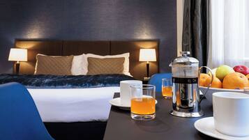 A hotel room with a bed, bedside lamps, a coffee maker, a fruit bowl, and a table with cups and a glass of tea.