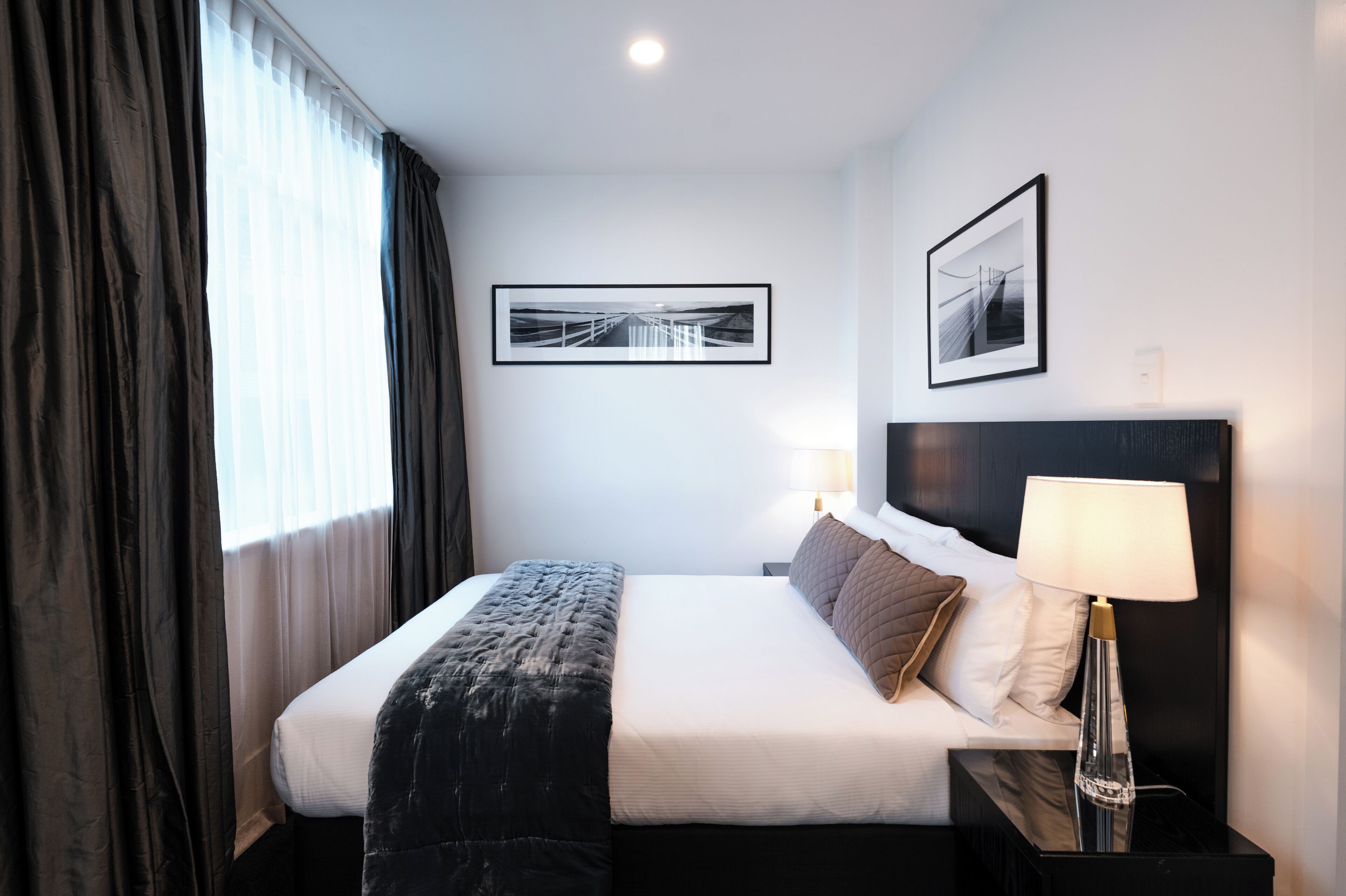 A hotel room with a neatly made bed, a bedside lamp, and two framed pictures on the wall.