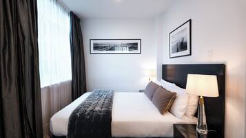 A hotel room with a neatly made bed, a bedside lamp, and two framed pictures on the wall.