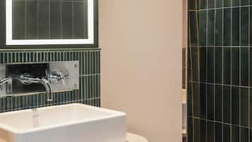 Un baño con lavamanos blanco, un espejo y zona de ducha.