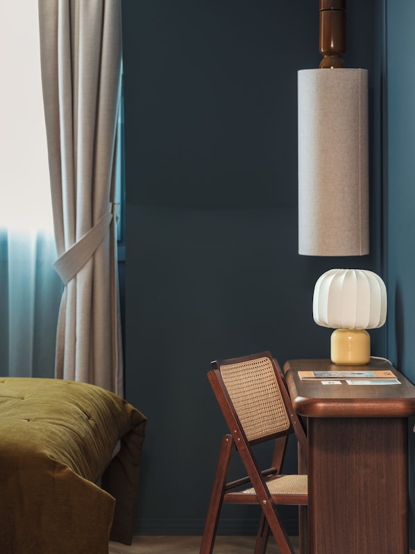A room with a bed, a chair, a table with a lamp, and a wall-mounted lamp. - Lazare Nomade (Paris)