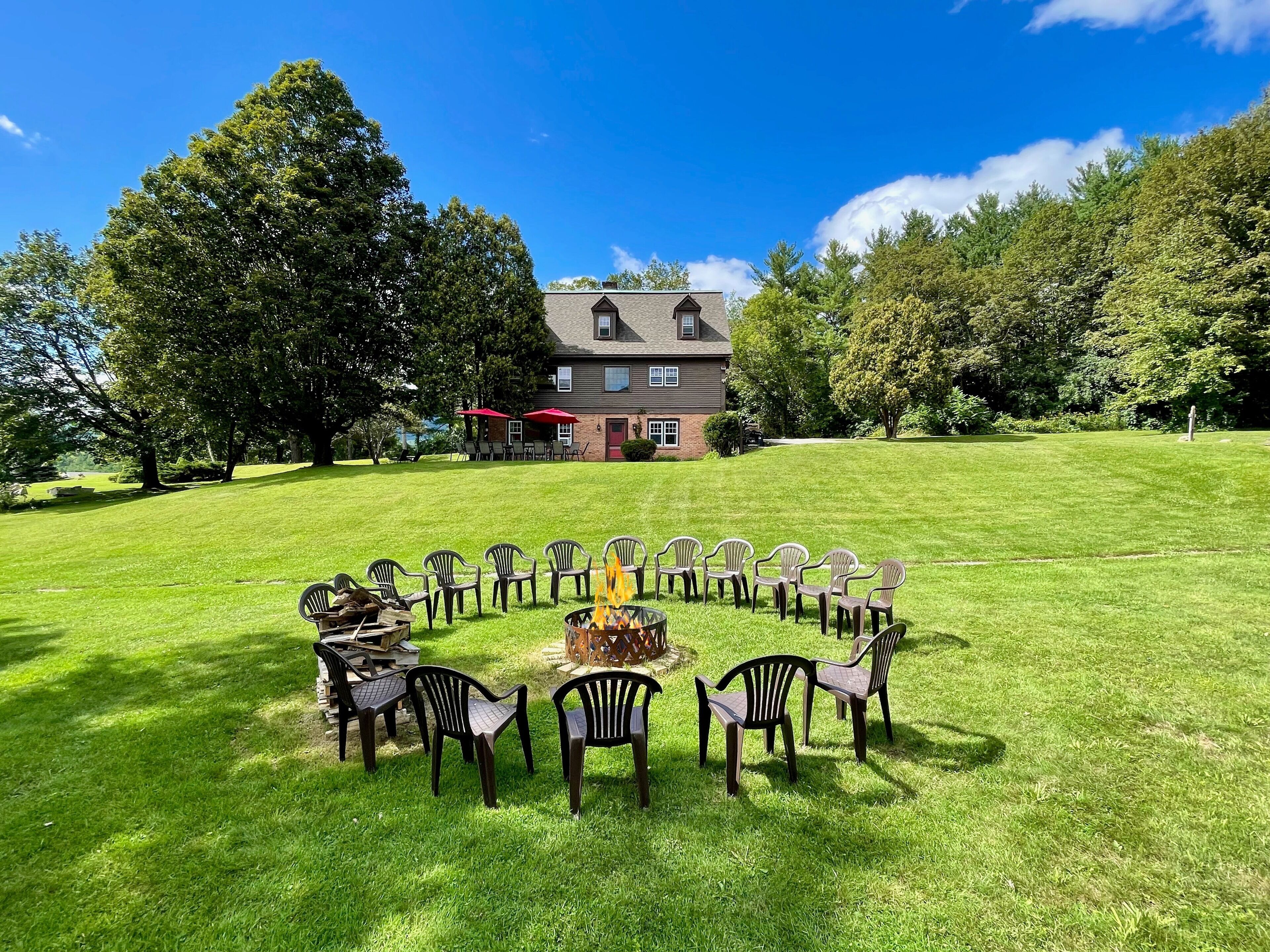 A circular arrangement of chairs around a fire pit on a grassy lawn, with a house and trees in the background.