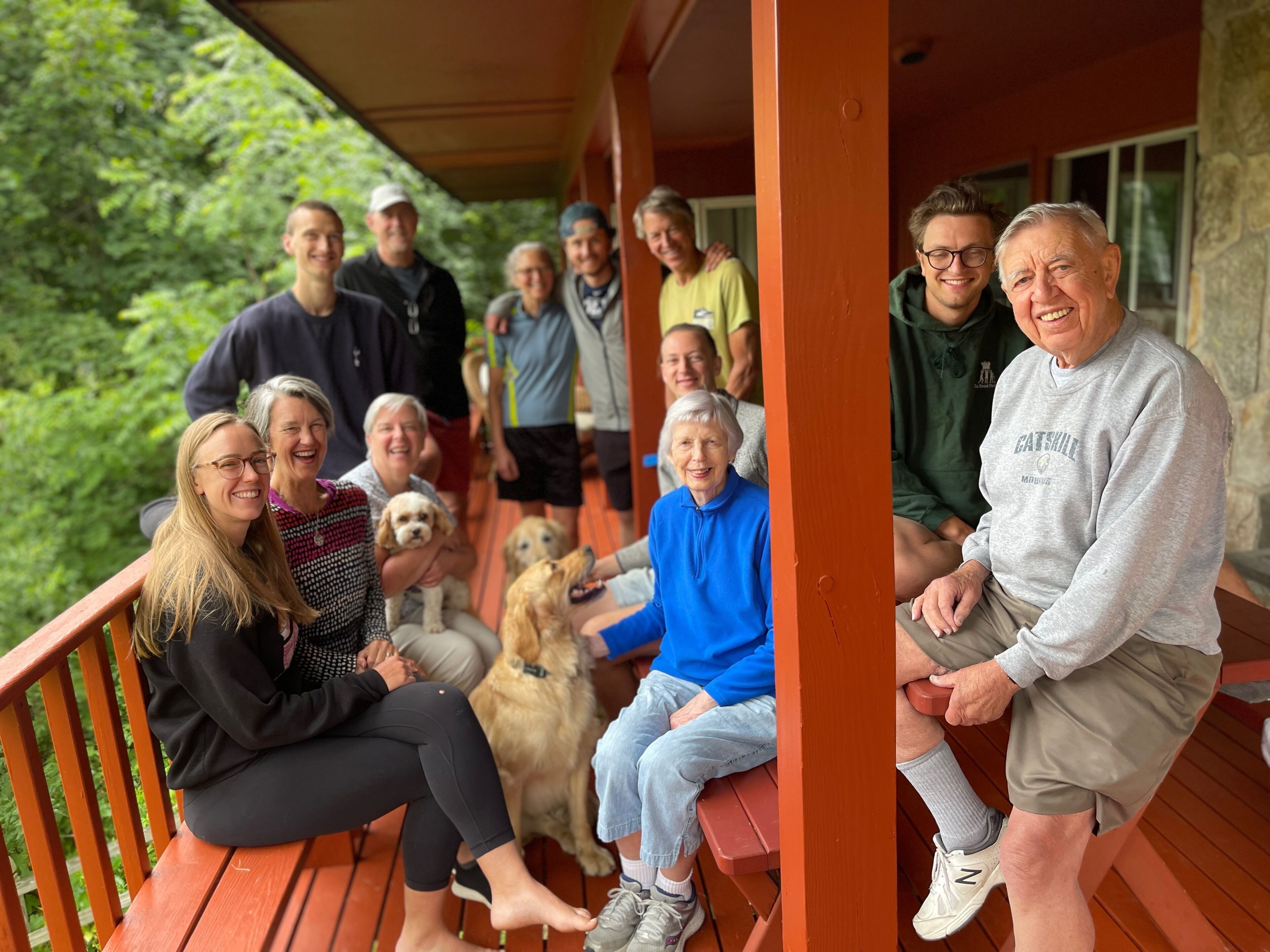 A group of people on a wooden deck with a stone wall and greenery in the background.
