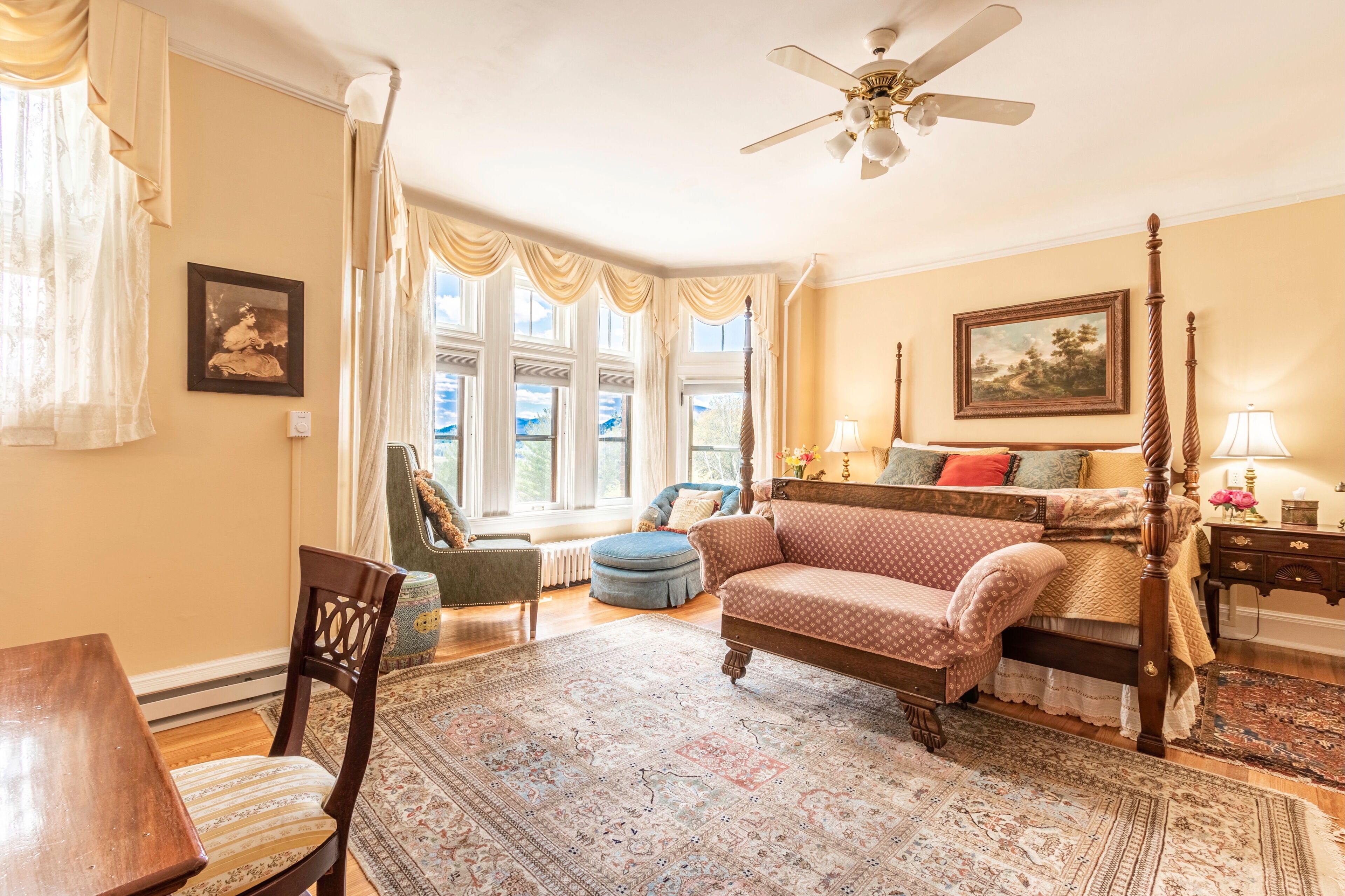 A bedroom with a large bed, a wooden chair, a table, and a window with curtains.