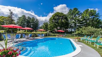 Relax by the pool surrounded by lush greenery and trees, with lounge chairs and umbrellas providing shade.