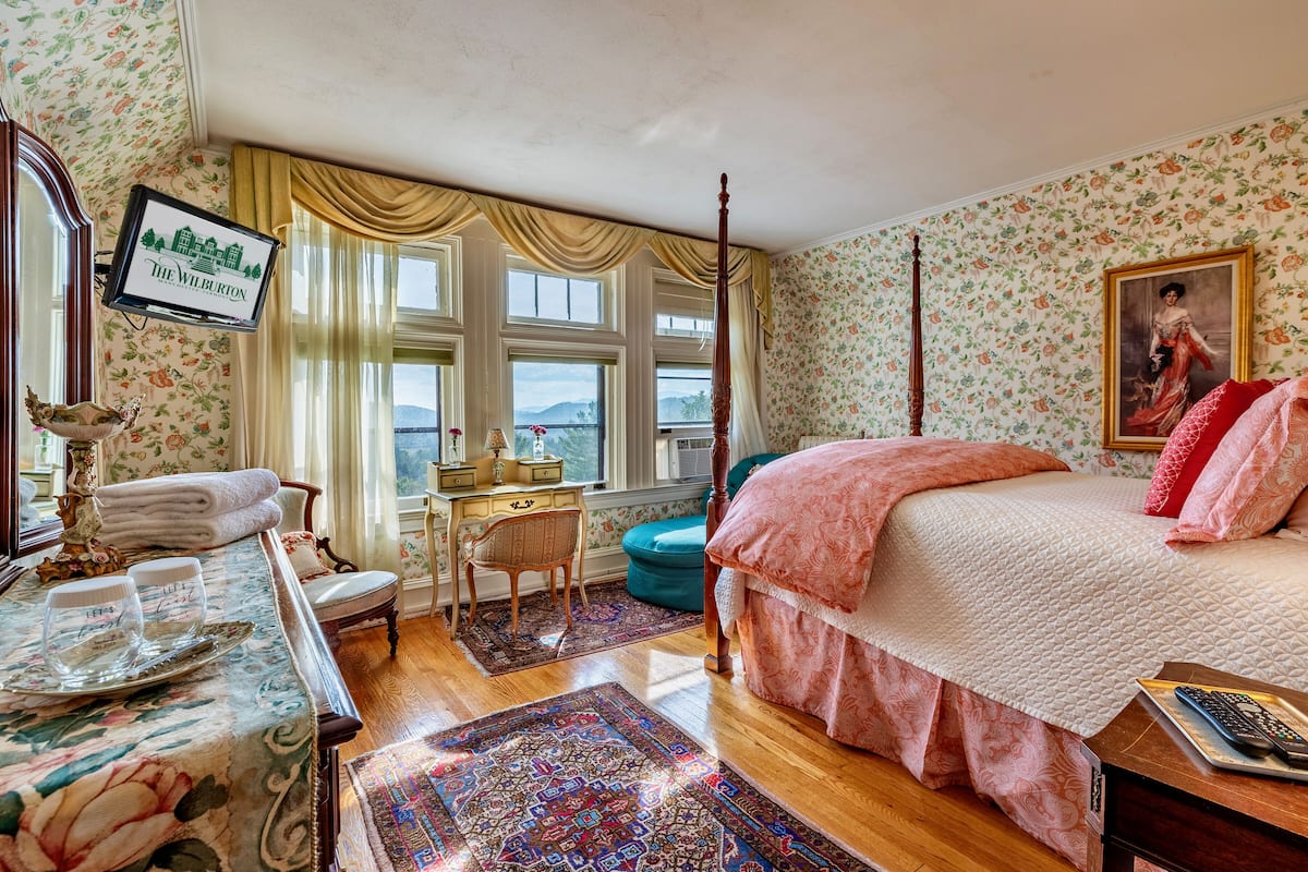 Ein Schlafzimmer mit Bett, Schreibtisch, Stuhl, Fernseher und Blick ins Freie.