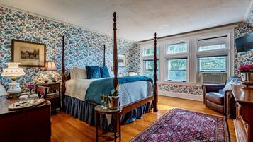 Ein Schlafzimmer mit einem Himmelbett, floralem Wandpapier, einem großen Fenster und Holzboden.
