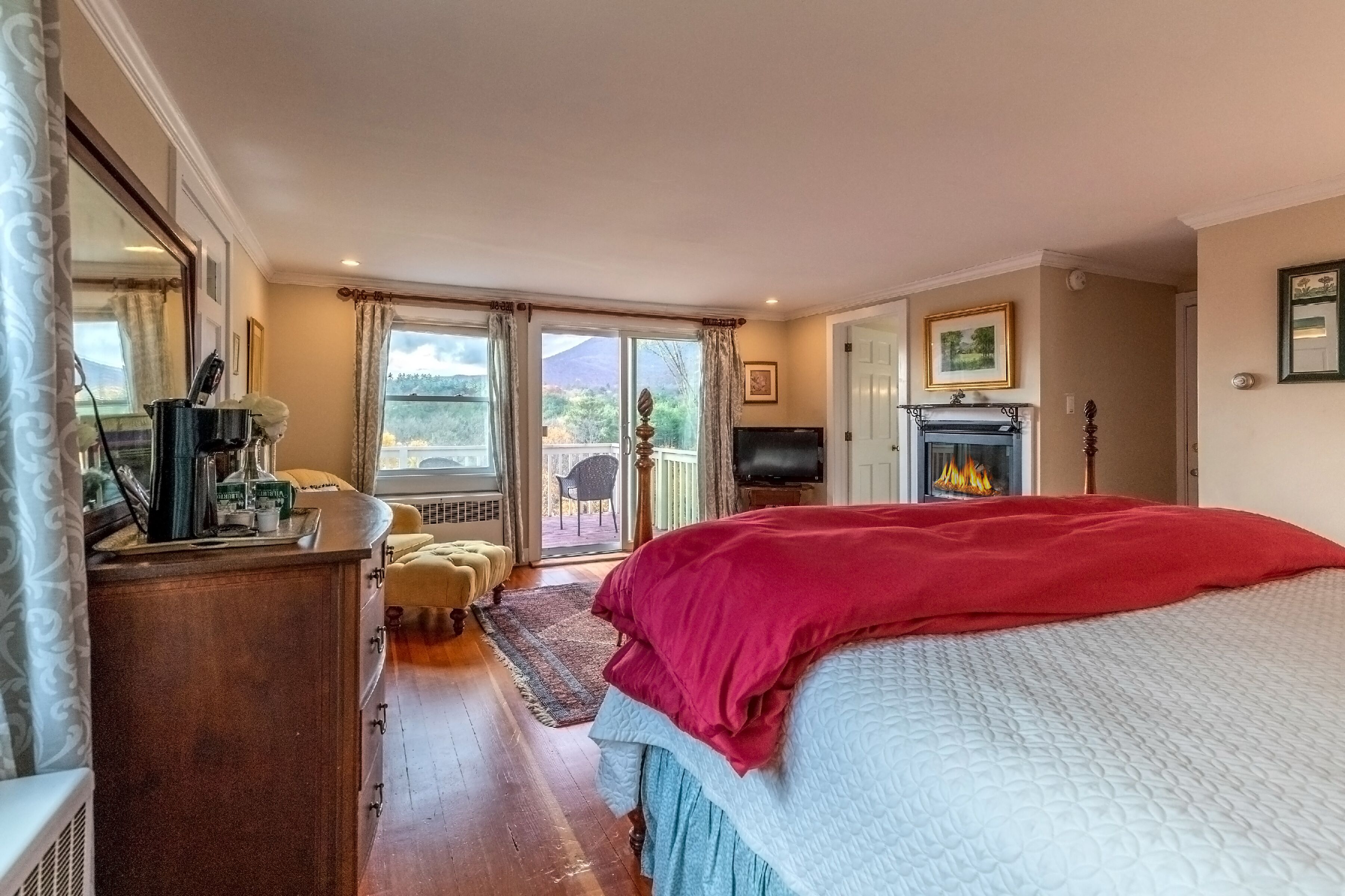 Ein Schlafzimmer mit einem großen Bett, einem Kamin, einem Fernseher und Blick ins Freie.