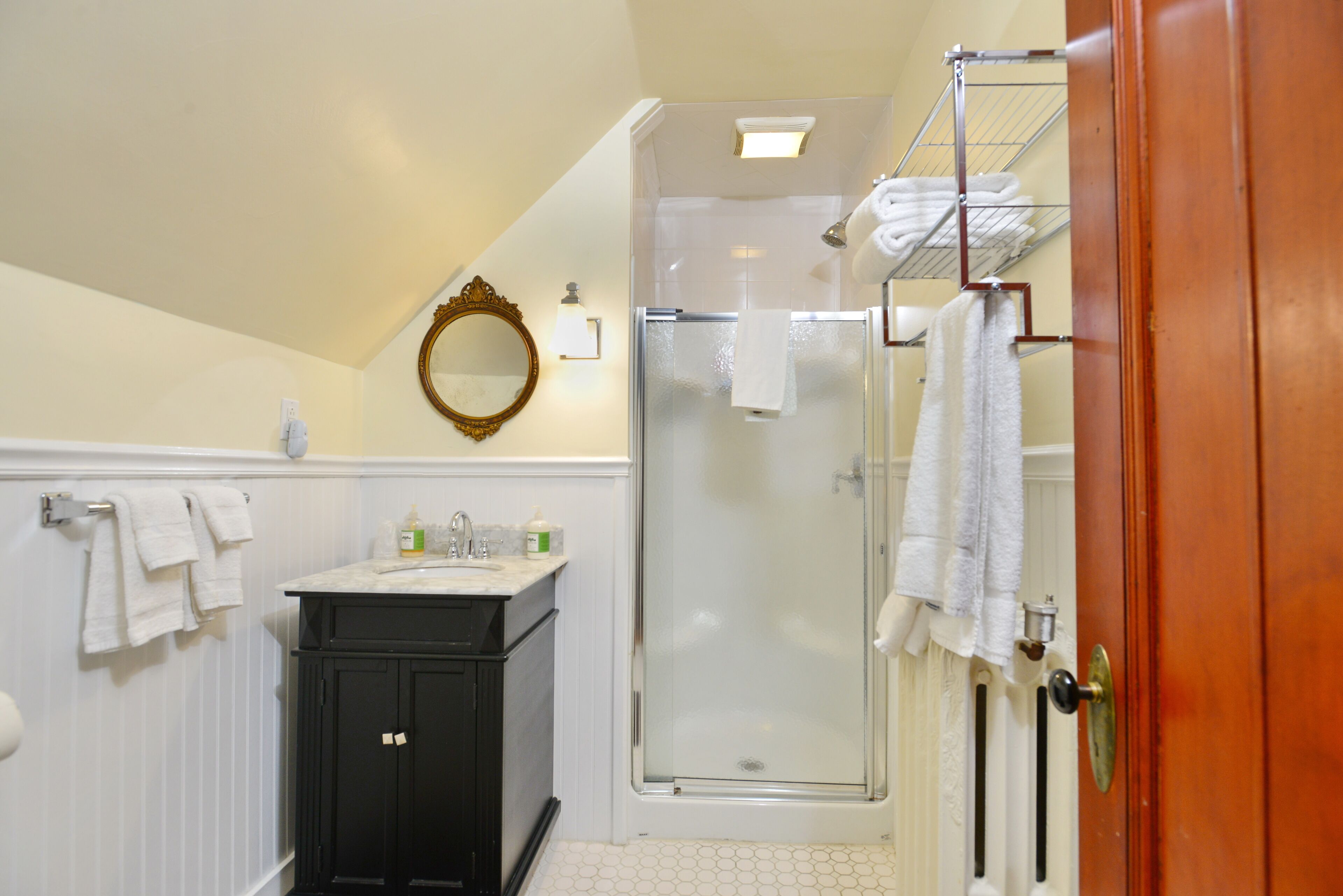 A bathroom with a sink, mirror, towel rack, and a glass-enclosed shower.