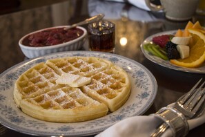 A plate of waffles with powdered sugar and a slice of butter on a floral-patterned plate.