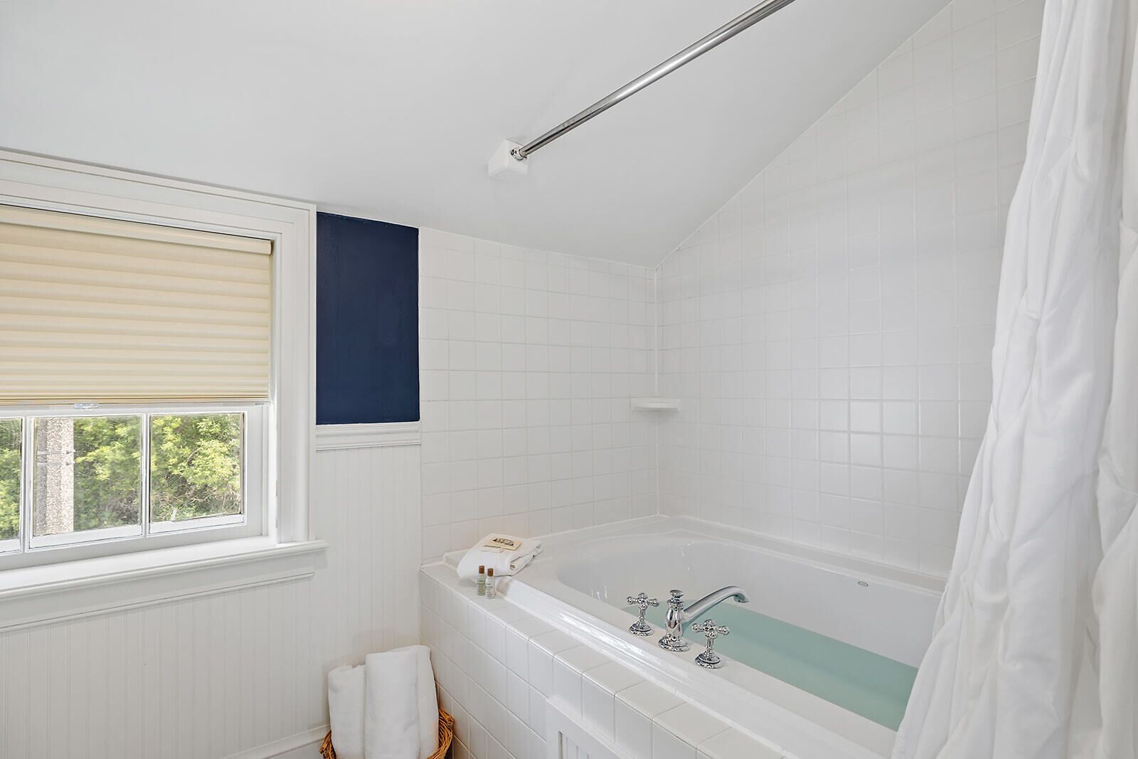A bathroom with a bathtub, a window with blinds, and a shower curtain.