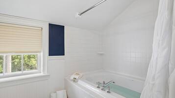 A bathroom with a bathtub, a window with blinds, and a shower curtain.