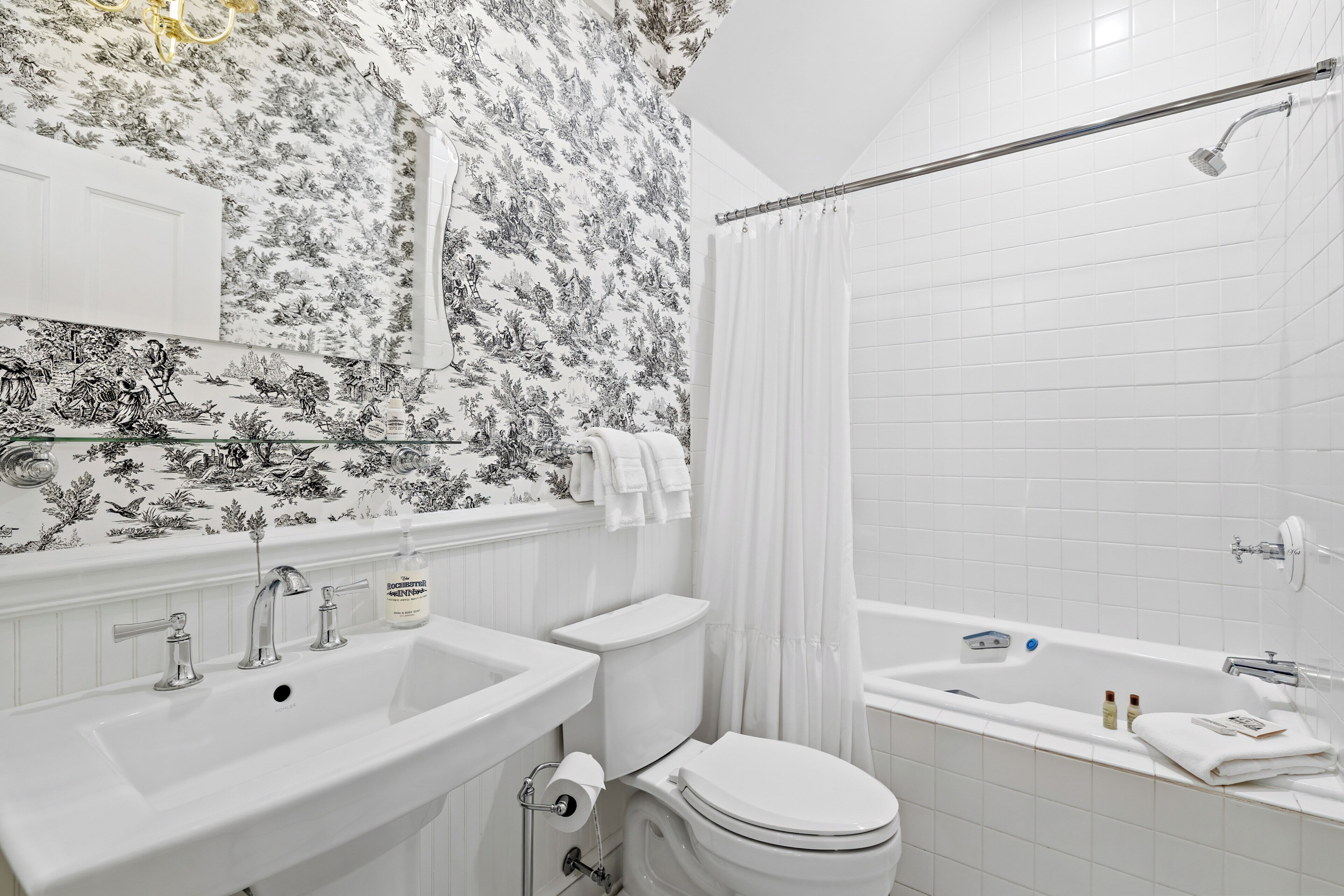 Une salle de bain équipée d’un lavabo, de toilettes et d’une baignoire, avec un papier peint à motifs floraux.