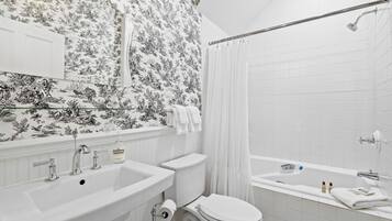 Une salle de bain équipée d’un lavabo, de toilettes et d’une baignoire, avec un papier peint à motifs floraux.