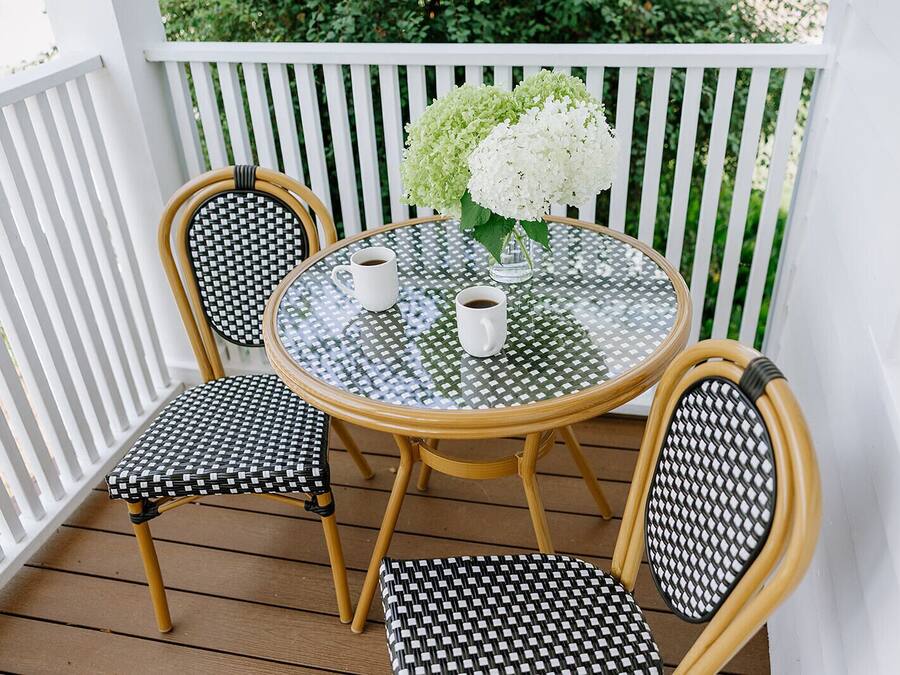 A round glass table with two chairs, each with a black and white woven seat and backrest, and a white vase with white flowers on the table.