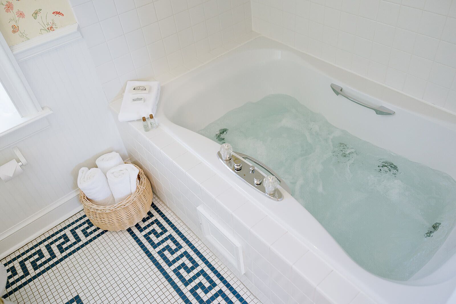 A bathroom with a bathtub, a wicker basket with towels, and a checkered floor.