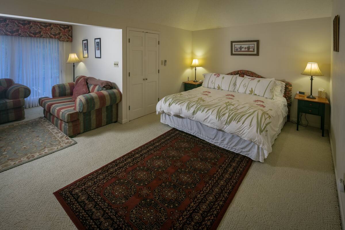 A bedroom with a large bed, two bedside tables with lamps, a sofa, a carpet, and a door.