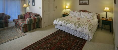 A bedroom with a large bed, two bedside tables with lamps, a sofa, a carpet, and a door.
