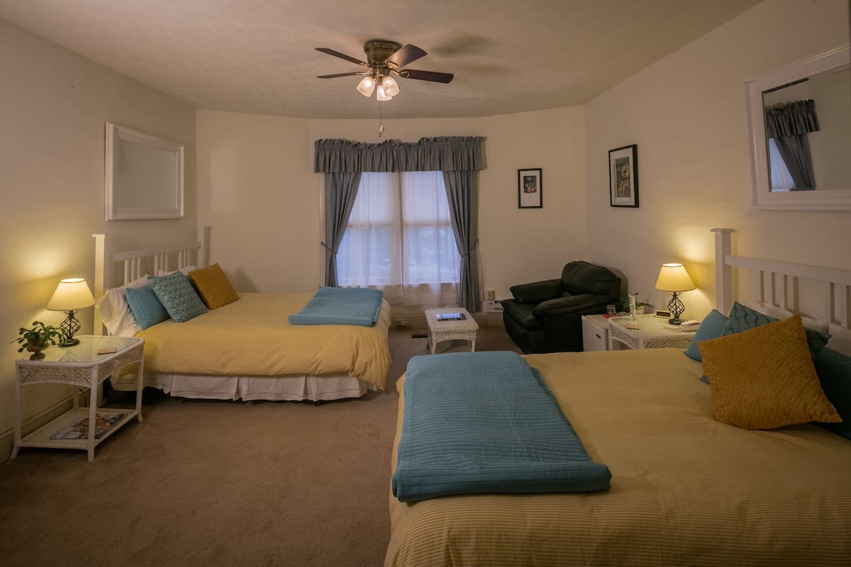 A bedroom with two beds, a ceiling fan, a window with curtains, and bedside lamps.