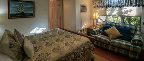 A bedroom with a bed, a sofa, a painting, a window with curtains, and a skylight.