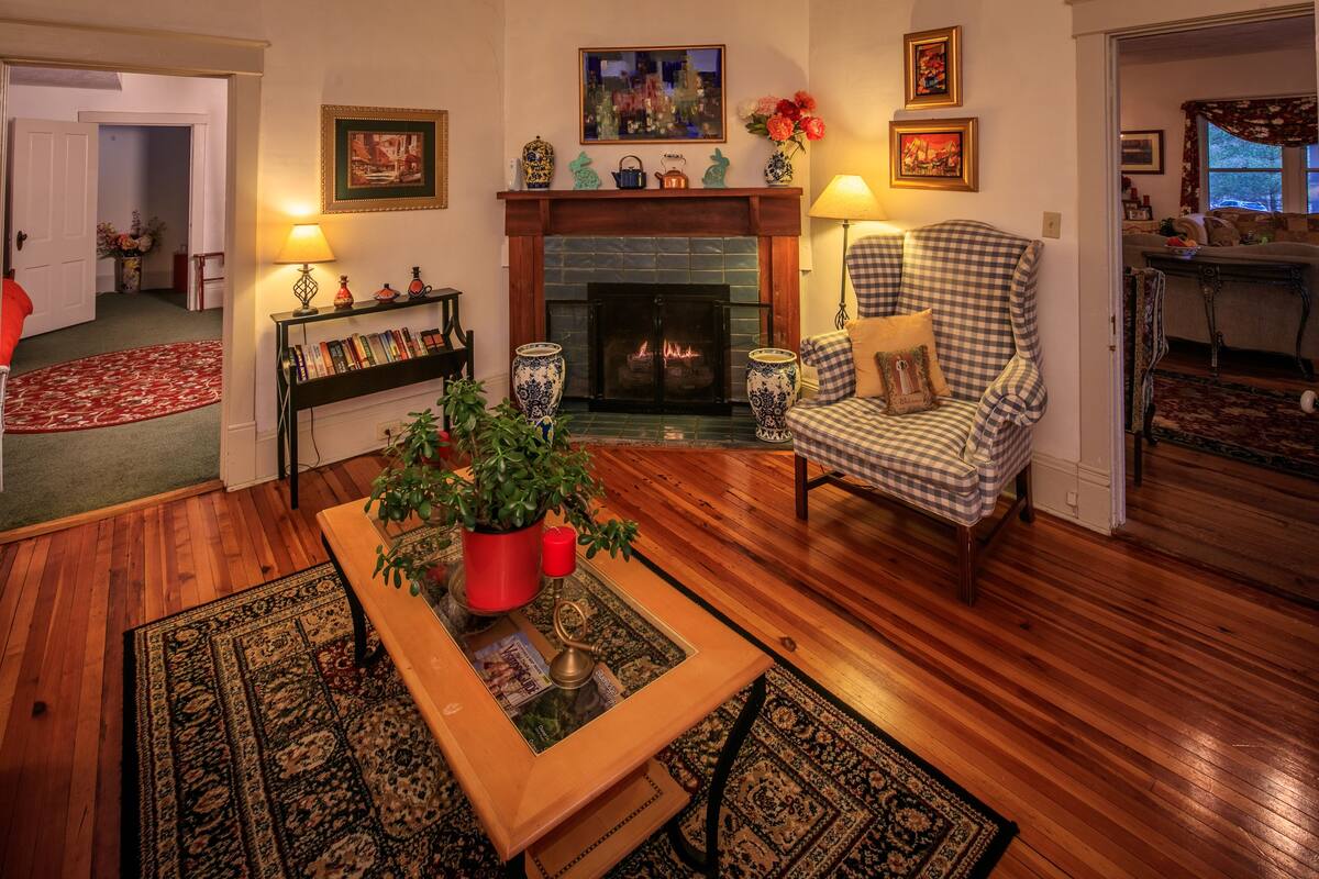 A cozy living room with a fireplace, a checkered armchair, a wooden coffee table, and a bookshelf.