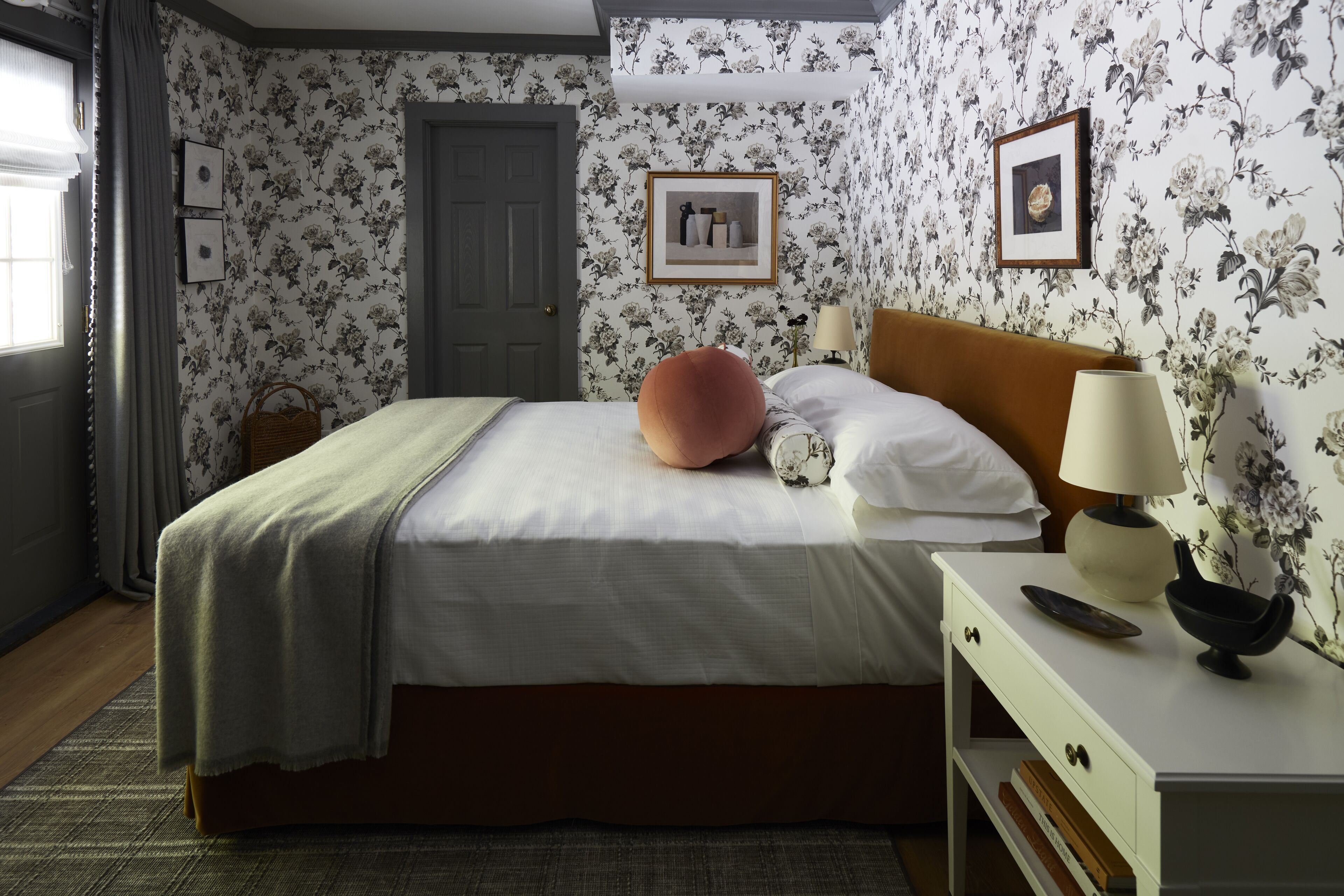 A bedroom with a bed, a nightstand, a lamp, and floral wallpaper.