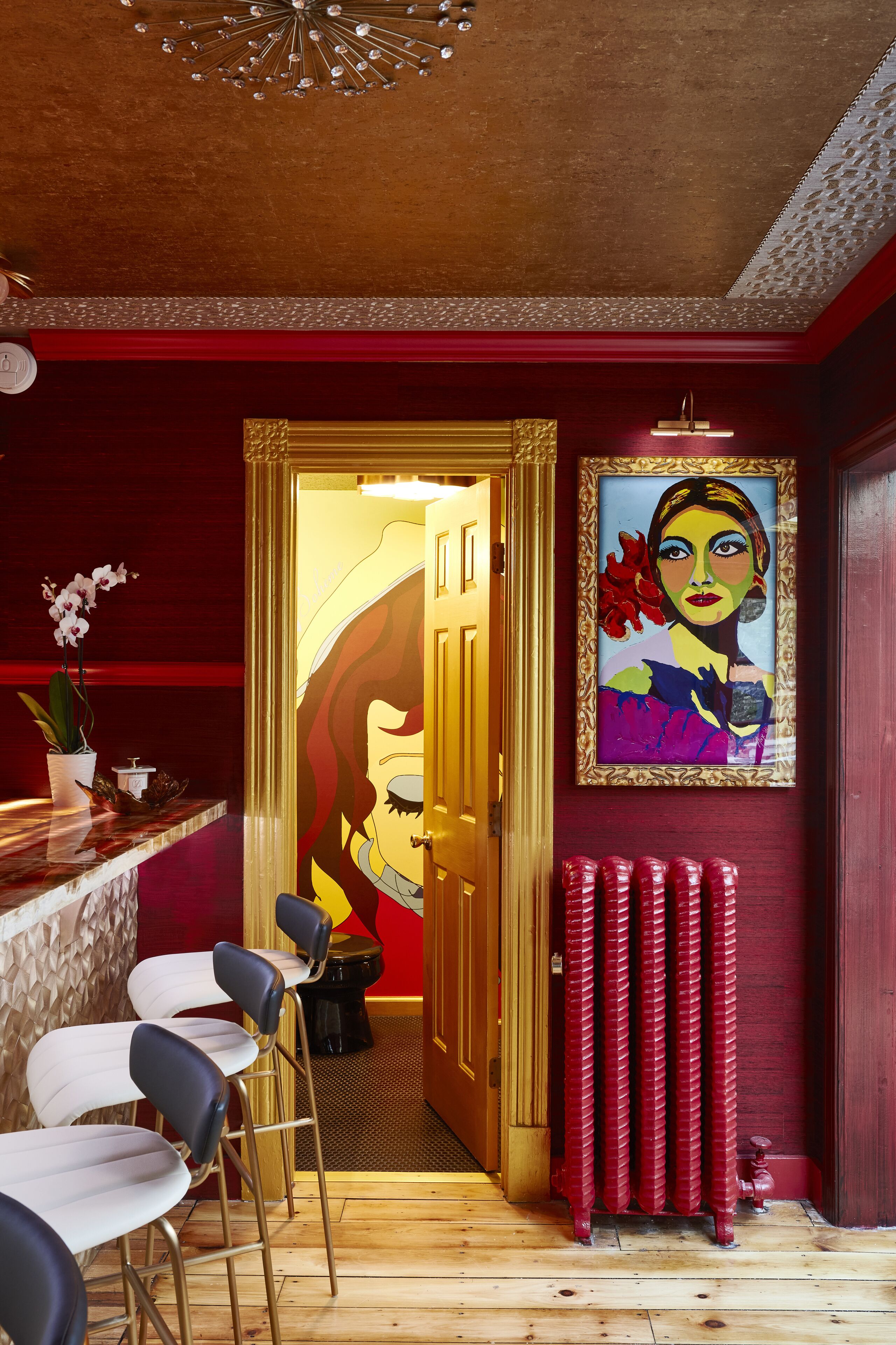 Angolo bar con arredamento nei toni del rosso e dell'oro, un'opera d'arte incorniciata e un pavimento in legno.